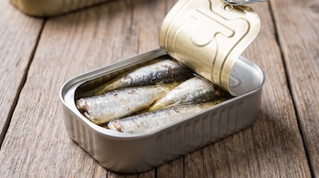 Lata metálica abierta con varias sardinas enteras en aceite sobre una tabla de madera con vetas.
