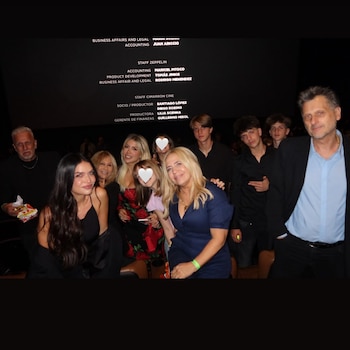 Un grupo de adultos y jóvenes posa en una sala de cine frente a una pantalla con nombres del equipo de producción en letras blancas