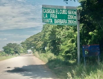 Vista de una carretera rural con un cartel verde a la derecha que muestra las distancias a Casigua El Cubo, La Fría y Santa Bárbara, rodeada de árboles