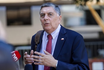 Un hombre con traje azul, corbata roja y un pin de la bandera de Chile gesticula ante un micrófono del canal TVN