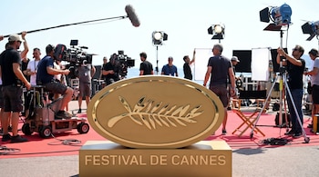 La Palma de Oro del Festival de Cannes en primer plano, con un equipo de filmación completo, cámaras, luces y boom de micrófono visibles en una alfombra roja.