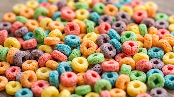 Piezas de cereal de colores rojo, amarillo, naranja, verde, azul y morado con forma de argolla dispersas en primer plano.