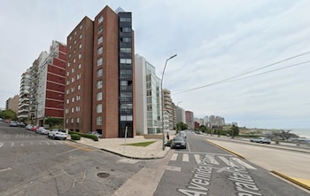 Un edificio de ladrillo en una esquina de una avenida costera con autos estacionados y vista al mar