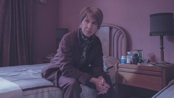 Mercedes Morán sentada en el borde de una cama con las manos entrelazadas, junto a una mesa de noche con frascos de medicamentos