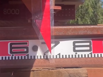 Una flecha roja apunta a una regla graduada con números sobre una estructura de metal oxidado