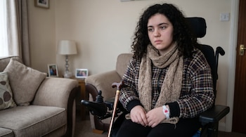 Mujer mexicana joven con cabello rizado oscuro sentada en una silla de ruedas eléctrica. Viste chaqueta a cuadros y bufanda, con una pulsera de alerta médica.
