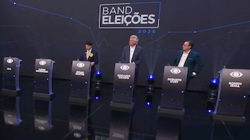Tres hombres permanecen de pie detrás de atriles frente a un fondo negro con la frase Band Eleições 2026 en un estudio iluminado