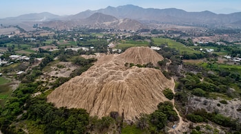 Vista aérea de un promontorio de barro erosionado rodeado de árboles verdes, campos agrícolas y montañas al fondo.