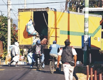 Dos camiones amarillos estacionados en una calle con trabajadores que descargan bultos y un hombre en primer plano