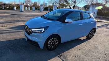 Un automóvil compacto de color azul claro se encuentra estacionado en una playa de estacionamiento pavimentada