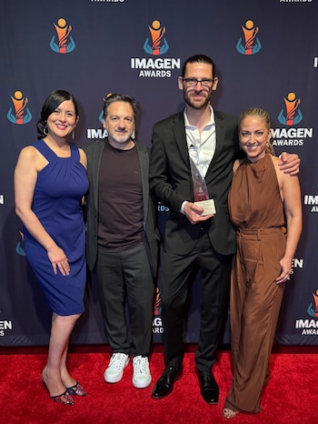 Cuatro personas posan en una alfombra roja frente a un fondo con logotipos de los Premios Imagen mientras un hombre sostiene un trofeo