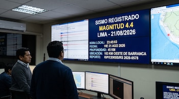 Dos hombres observan pantallas gigantes con datos técnicos de un reporte sísmico, sismogramas y un mapa de Perú.