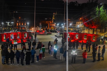 Un grupo de ciudadanos y agentes de policía con chalecos reflectantes permanecen reunidos de noche en una plaza iluminada