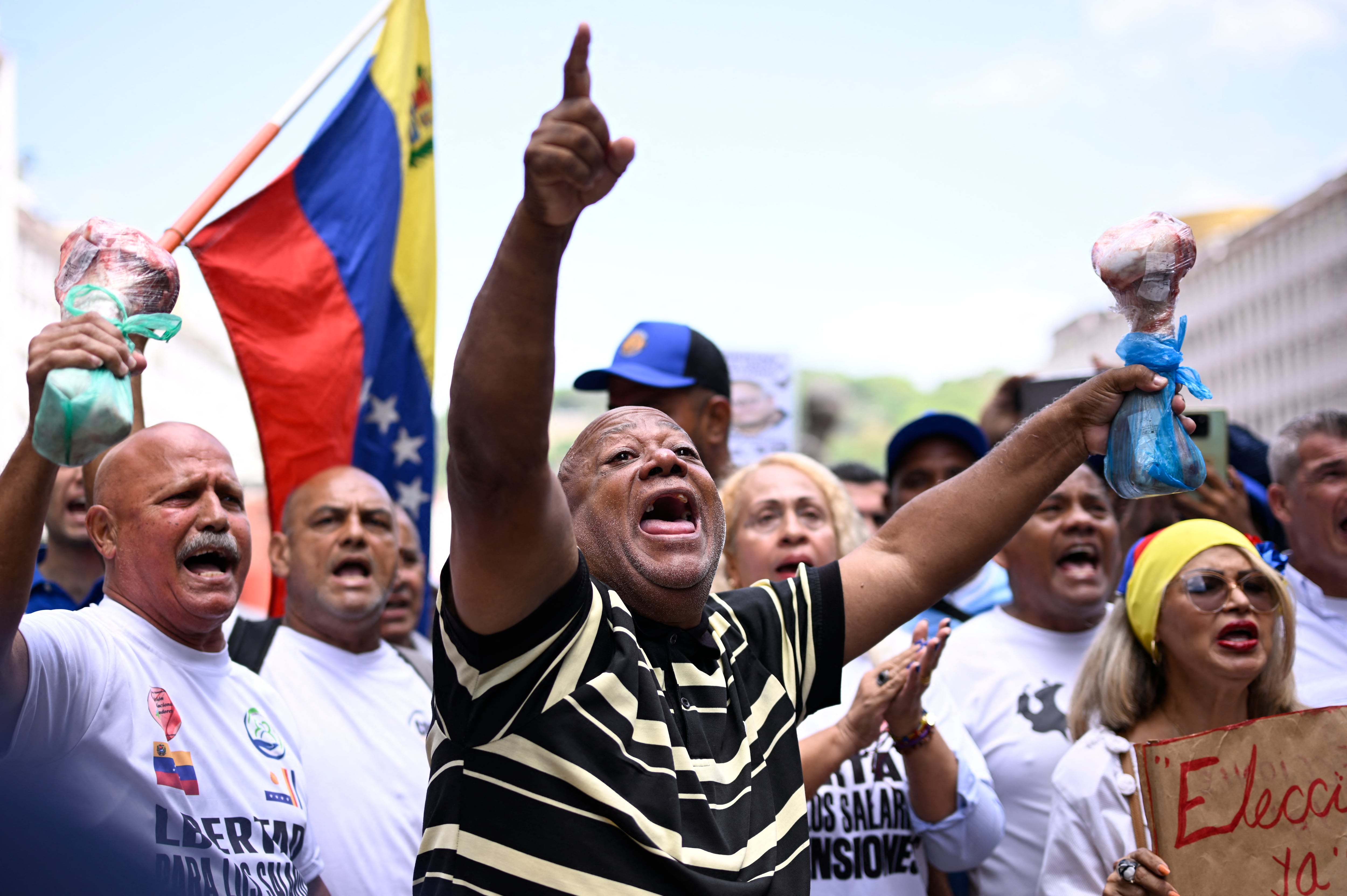 Los trabajadores sindicalizados corean consignas mientras sostienen huesos de vaca durante una manifestación en la que reclaman mejores condiciones laborales y elecciones presidenciales, frente al Consejo Nacional Electoral (CNE) en Caracas, el 9 de junio de 2026. (Maxwell BRICENO / AFP)