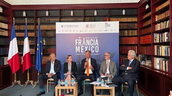 Cinco personas vestidas de traje están sentadas frente a un panel promocional en una sala con estanterías de libros y banderas de Francia y Europa.