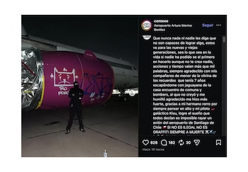 Una persona enmascarada de negro posa frente al motor de un avión de color púrpura, que ha sido vandalizado con grafitis blancos y azules