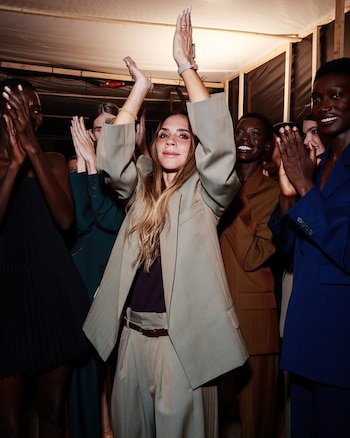 Victoria Beckham viste un traje holgado beige y aplaude con las manos levantadas junto a varias modelos que también aplauden