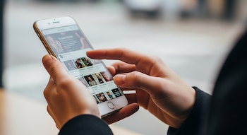 Primer plano de manos sosteniendo un smartphone blanco mientras se desplaza por una aplicación con imágenes de perfil.