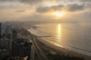 Vista panorámica de edificios altos junto a la playa y el mar donde se refleja el sol a través de las nubes.