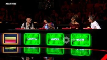 Cuatro personas sentadas en una mesa larga frente a pantallas LED verdes que muestran nombres como Jimena, en un estudio de televisión con un público oscuro al fondo