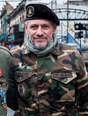 Primer plano de Daniel Ponce, un hombre de mediana edad con barba gris, ojos azules, boina negra, pañuelo y chaqueta de camuflaje con insignias militares