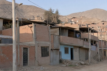 Casas de ladrillo visto con grietas en los muros junto a una calle de tierra y cerros áridos al fondo.