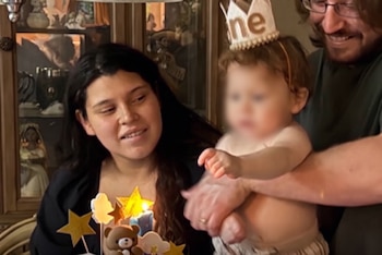 Una mujer y un hombre sostienen a un niño con corona de cumpleaños frente a un pastel decorado con estrellas y un oso