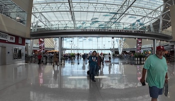 Interior de la terminal del Aeropuerto Internacional de Indianápolis con techo de cristal, estructuras metálicas y personas caminando sobre suelo brillante