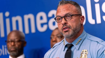 Primer plano de Brian O'Hara, jefe de la policía de Minneapolis, con barba y gafas, hablando en un podio con un fondo azul que dice 'Minneapolis'