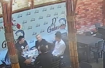 Varias personas sentadas alrededor de una mesa en el interior de un restaurante frente a una pared con un logotipo
