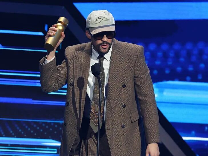 El saco marrón de cuadros con corbata de patrón geométrico y gorra gris revela el gusto de Bad Bunny por los detalles clásicos y los accesorios distintivos en sus apariciones públicas (@LatinBillboards/X)