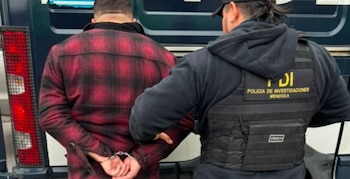 Hombre esposado con camisa a cuadros roja y negra junto a un agente de policía con chaleco táctico que dice PDI Policía de Investigaciones Mendoza