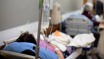 Primer plano de un paciente en cama de hospital recibiendo suero intravenoso. Se ven la bolsa de fluidos y el brazo del paciente