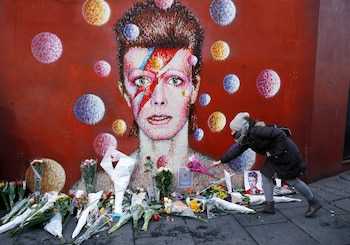 FILE PHOTO: A woman leaves a bouquet at a mural of David Bowie in Brixton, south London, January 11, 2016. David Bowie, a music legend who used daringly androgynous displays of sexuality and glittering costumes to frame legendary rock hits "Ziggy Stardust" and "Space Oddity", has died of cancer. REUTERS/Stefan Wermuth/File Photo