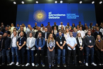 Una multitud de personas diversas, hombres y mujeres, de pie y sentadas en un auditorio. Al fondo, una pantalla azul con el Sol de Mayo y el texto 'el peronismo debate para ser alternativa nacional'