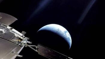 Vista del planeta Tierra parcialmente iluminado desde el espacio, con una parte de una nave espacial blanca en el lado izquierdo inferior