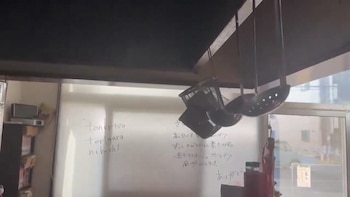 Cuchara coladora y cesta de metal cuelgan de ganchos en el techo de una cocina de restaurante, con un pizarrón blanco al fondo