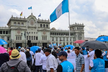 Una multitud con sombrillas y chalecos de Poder Ciudadano se reúne frente al Palacio Nacional de la Cultura bajo la bandera de Guatemala