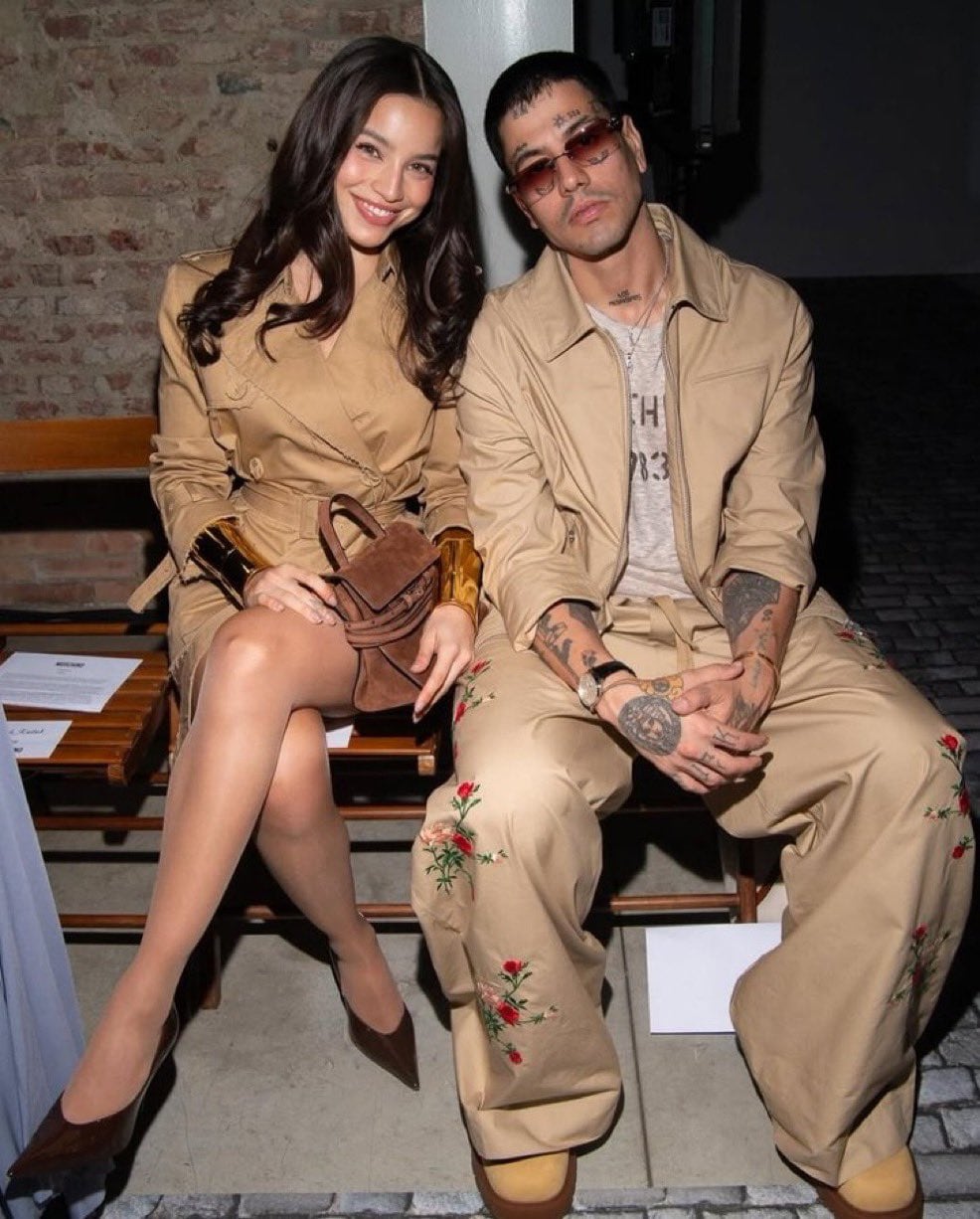 Los artistas Duki y Emilia posan sonrientes en la primera fila del desfile de Moschino durante la Semana de la Moda de Milán, luciendo elegantes atuendos