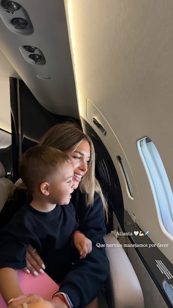 Mujer de cabello rubio sentada en avión con un niño pequeño, ambos mirando por la ventanilla. Interior de un avión privado con asientos beige y panel superior