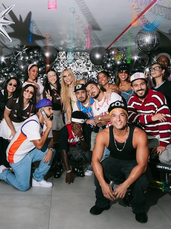 Grupo de personas, incluyendo Vinicius Jr., en una fiesta con decoración de globos plateados, bola de discoteca y espirales colgantes de colores