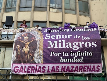 Balcón de un edificio con un cartel morado del Señor de los Milagros, adornos festivos y personas situadas en la parte superior