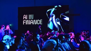 Vista de una audiencia en un evento con una gran pantalla que muestra 'AI IN FINANCE' y gráficos abstractos en tonos azules, iluminando el espacio