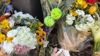 Ramos de flores de varios colores y dos pelotas de tenis con mensajes escritos colocados sobre el suelo