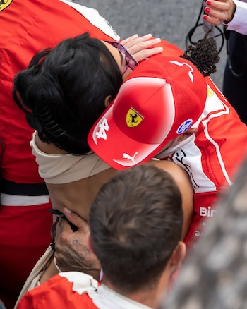 Lewis Hamilton con gorra y traje rojo de Ferrari, siendo abrazado por Kim Kardashian, vista de espaldas con cabello oscuro y top beige