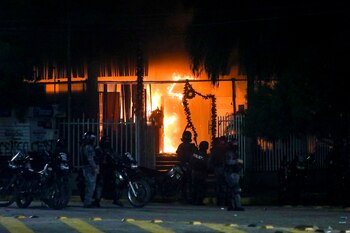Policías frente a una oficina gubernamental incendiada mientras partidarios de Luis Fernando Camacho, gobernador de la región de Santa Cruz, protestan en Santa Cruz, Bolivia, el miércoles 28 de diciembre de 2022. La policía detuvo a Camacho por cargos de presunto terrorismo con relación a la crisis de 2019. (AP Foto/Ipa Ibáñez)