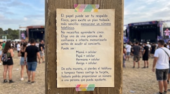 Un cartel de papel pegado con cinta adhesiva en un poste de madera ante el público de un concierto al aire libre.