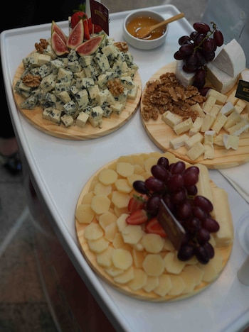 Tablas de madera con quesos en cubos, uvas rojas, higos, fresas y nueces. Un tazón de miel con cuchara sobre una bandeja blanca