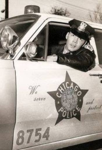 Fotografía en blanco y negro de un policía uniformado dentro de un patrullero con la insignia de la Policía de Chicago en la puerta