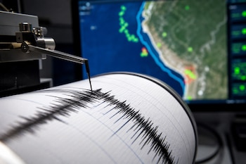 La aguja de un sismógrafo traza líneas sobre un tambor de papel frente a una pantalla con el mapa satelital de una costa.